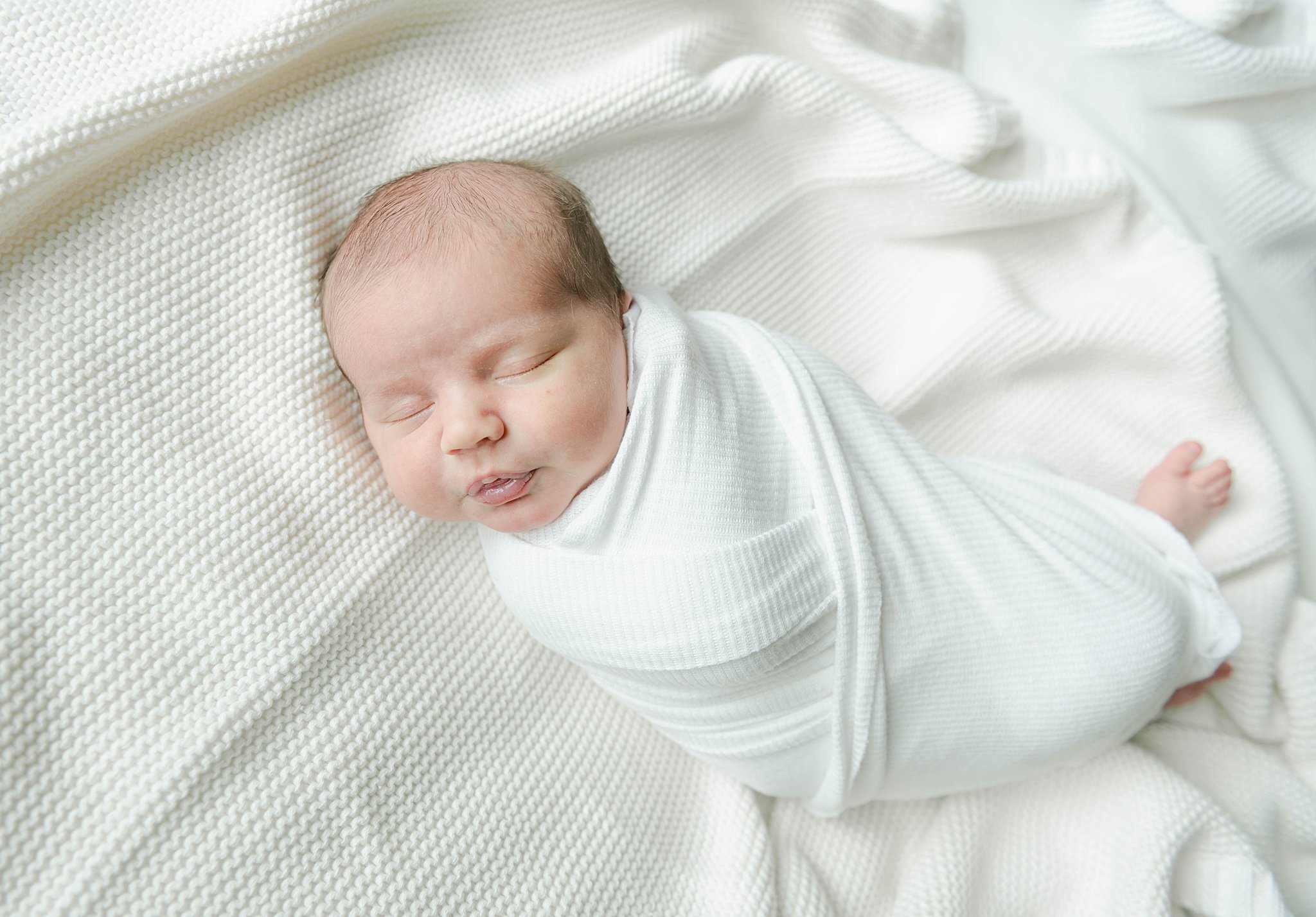 swaddled newborn sleeps on a bed of white blankets baby stores lancaster pa