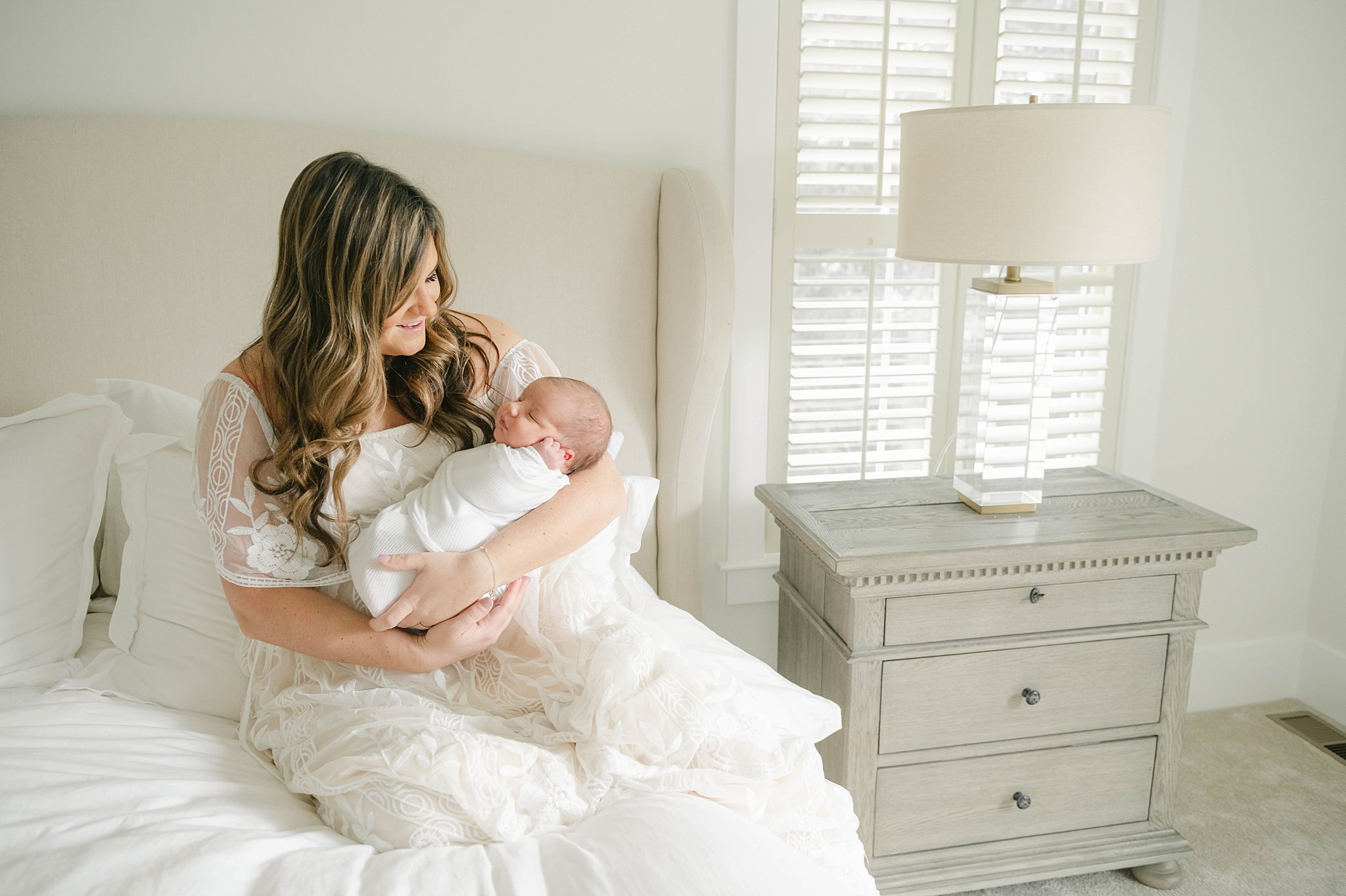 Mother in a white lace dress holds her newborn on a bed chester county hospital labor and delivery