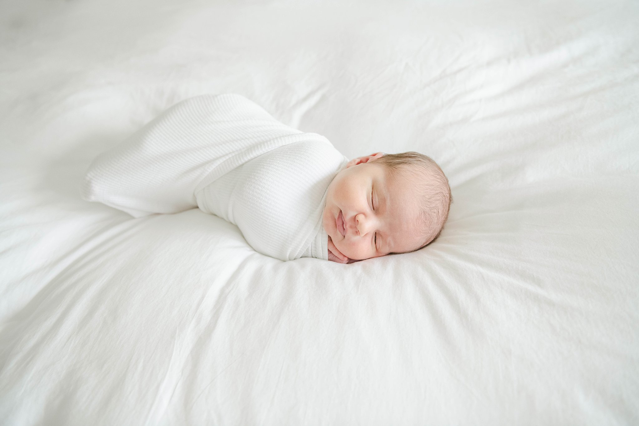 Newborn baby sleeps on their hands on a white bed chester county hospital labor and delivery