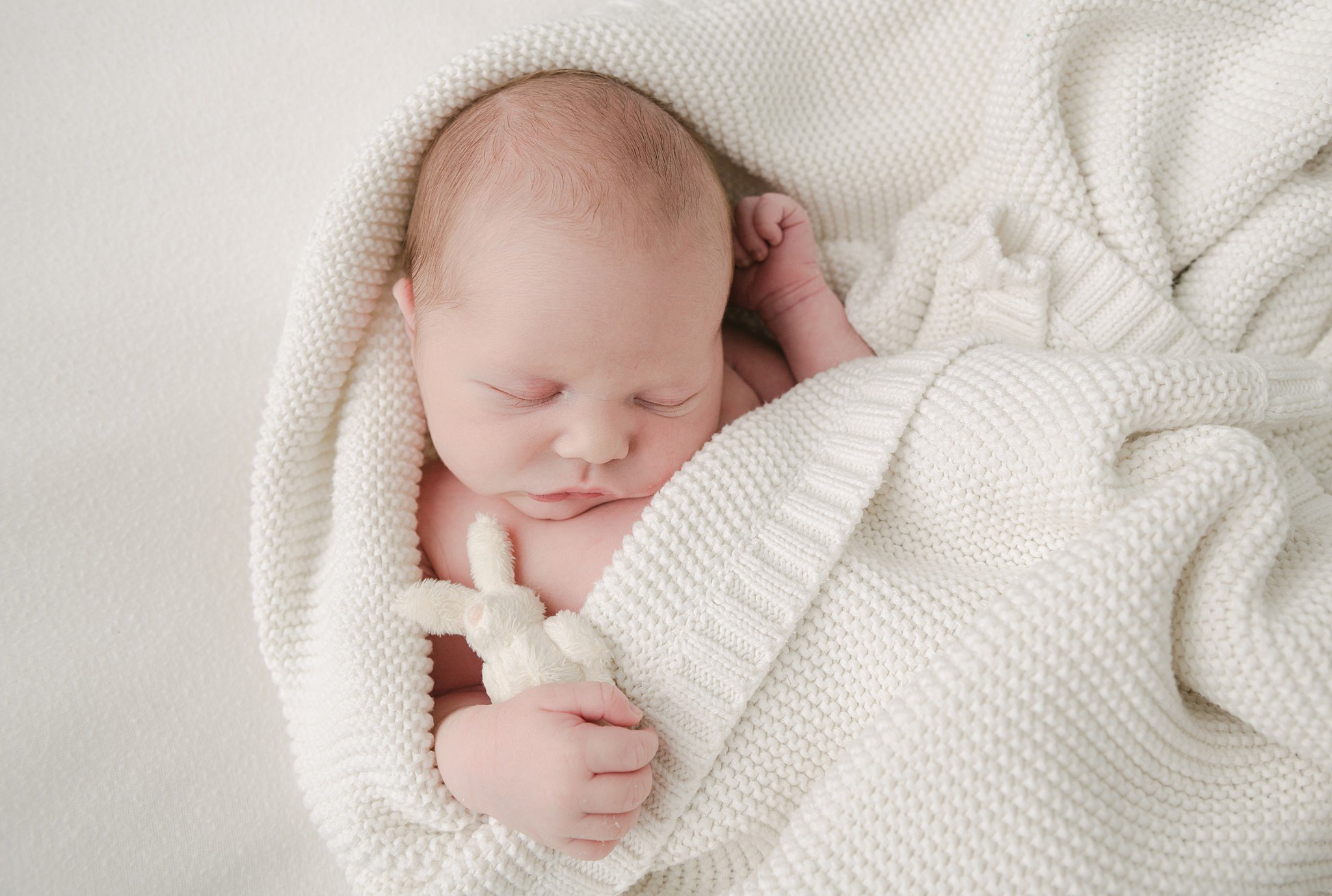 A newborn baby sleeps in a white blanket with a small stuffed bunny women and babies hospital lancaster