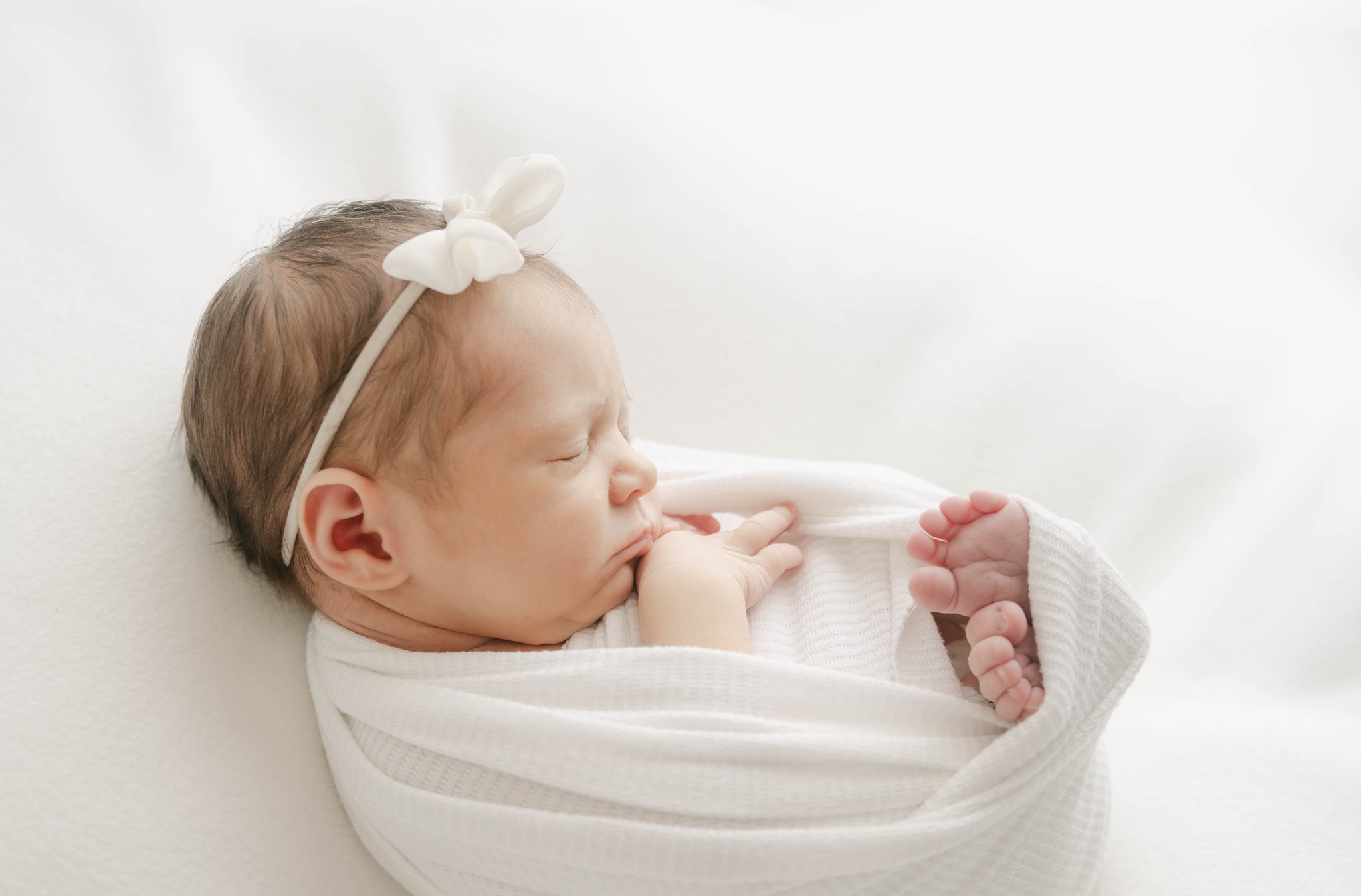 A newborn baby sleeps in a white swaddle with toes sticking out the bottom baby boutique west chester pa