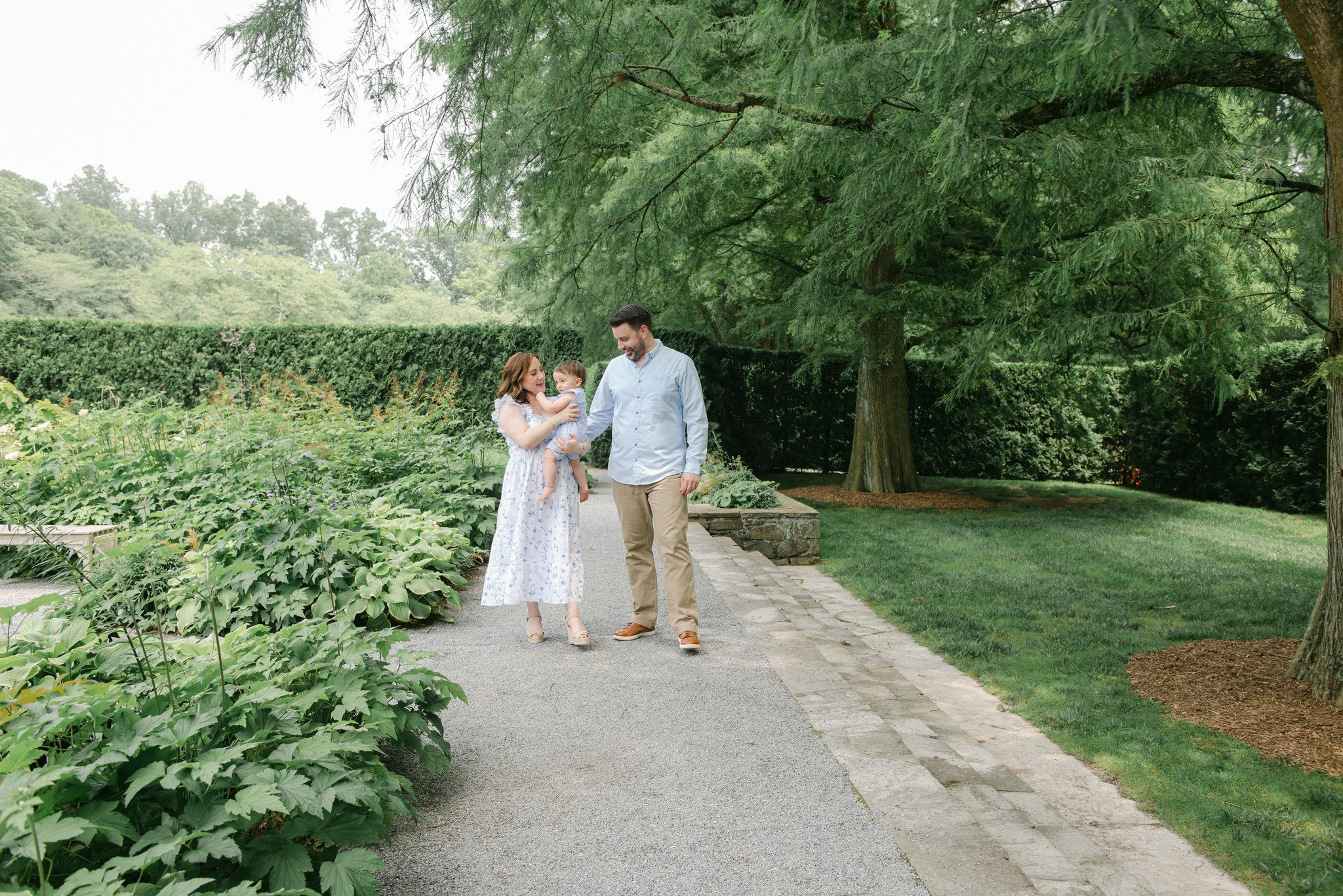 Parents walk through a garden on a gravel path while carrying their infant son chester county daycare