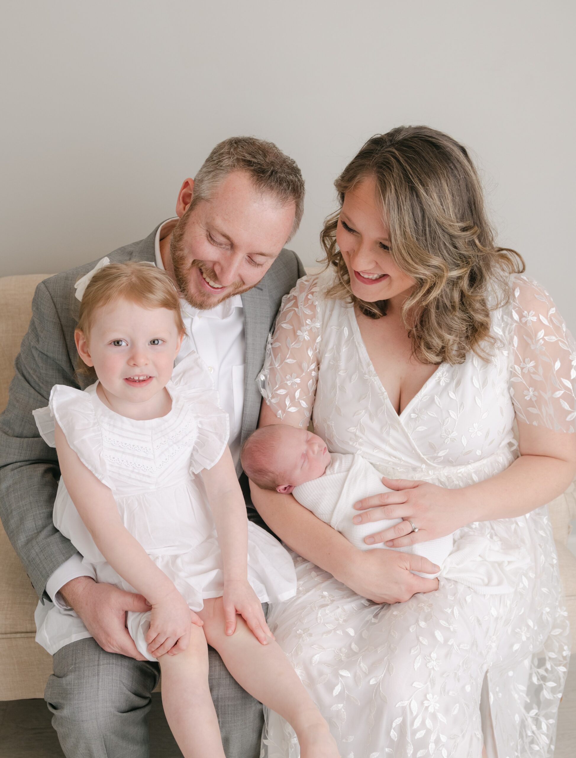 A family sits on a couch together with the newborn baby in mom's lap