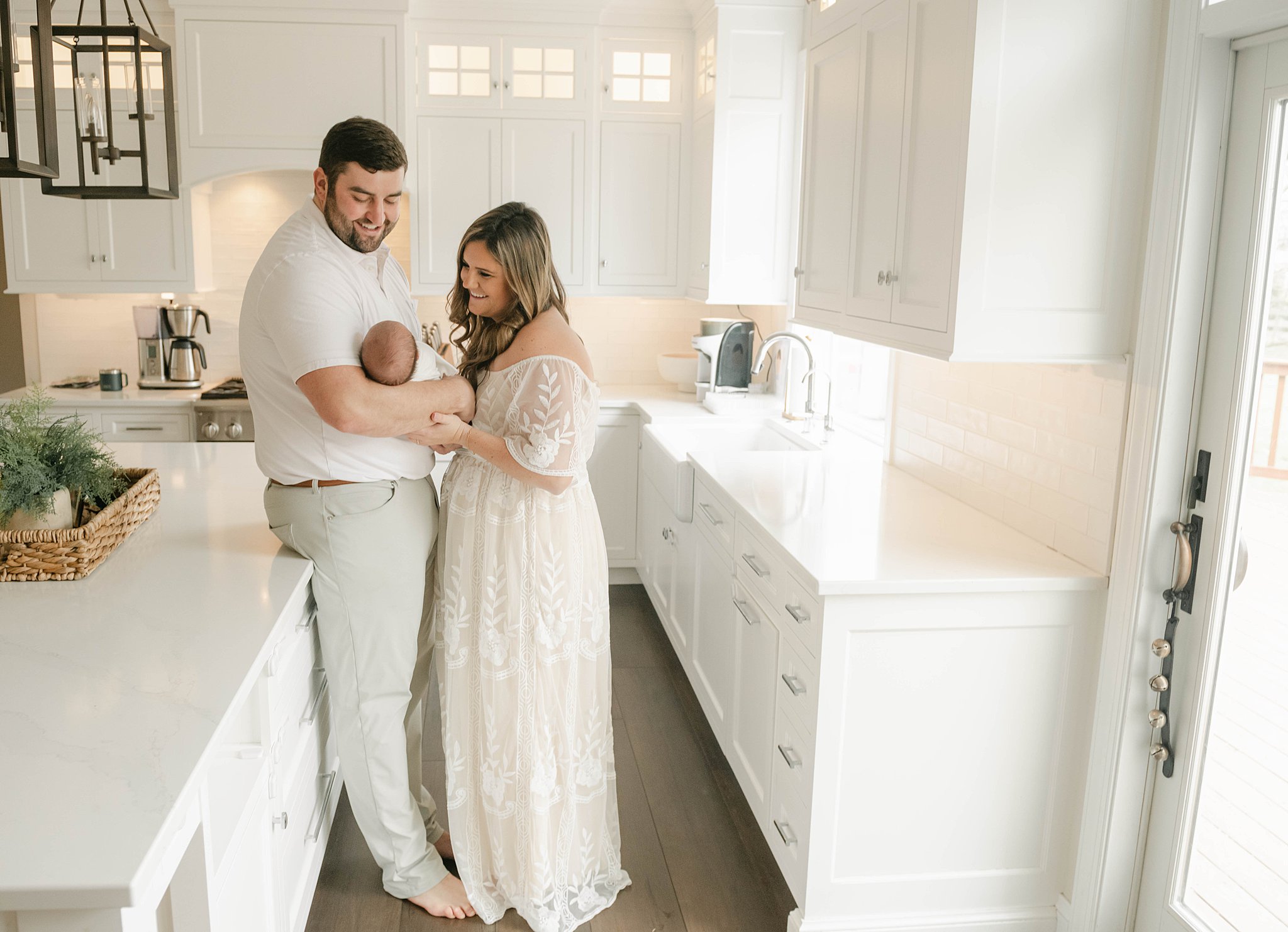 A mother and father lean together in the kitchen while their newborn baby sleeps in dad's arms prenatal massage west chester pa