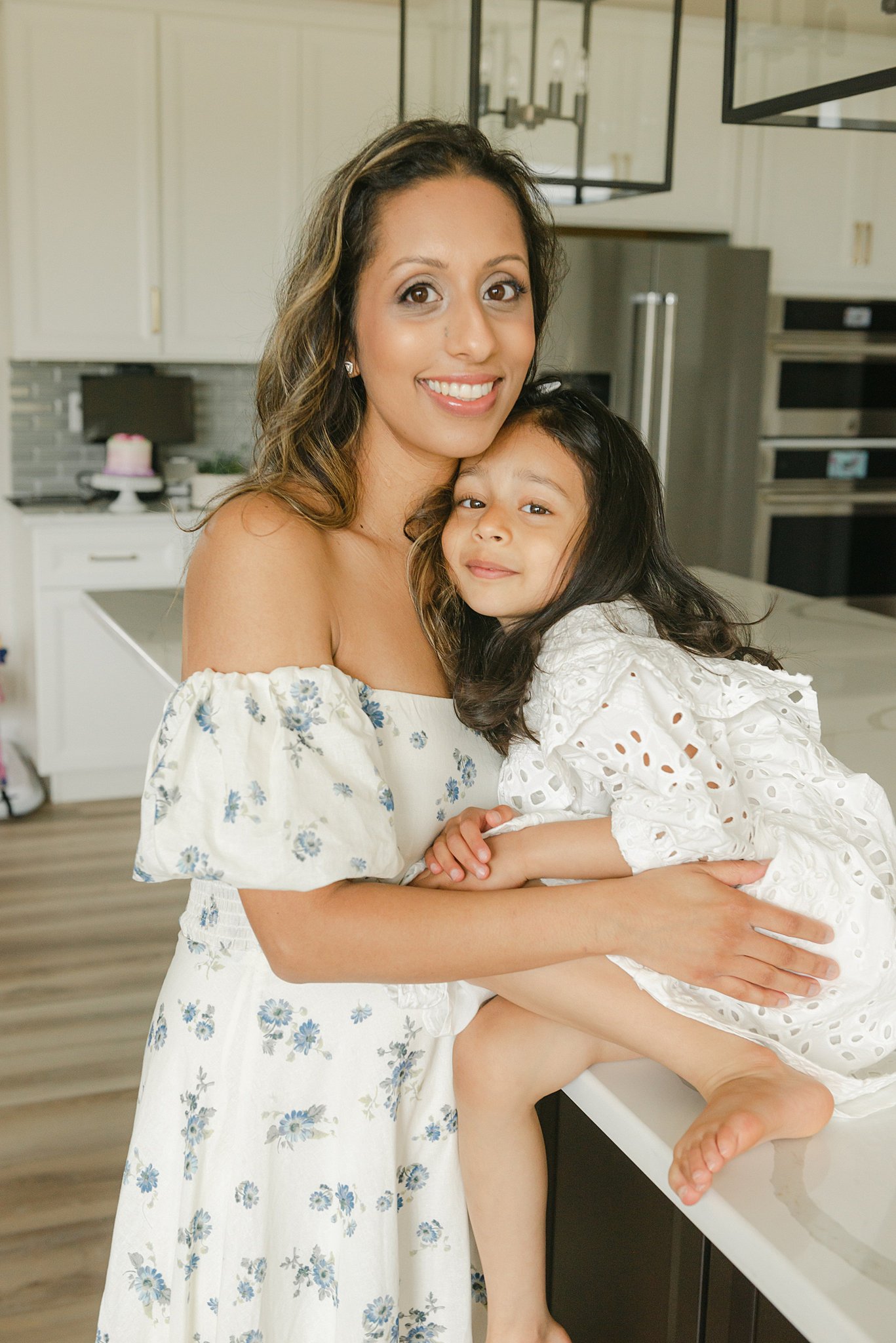 A mom in a floral dress hugs her young daughter sitting on the kitchen counter downington daycare