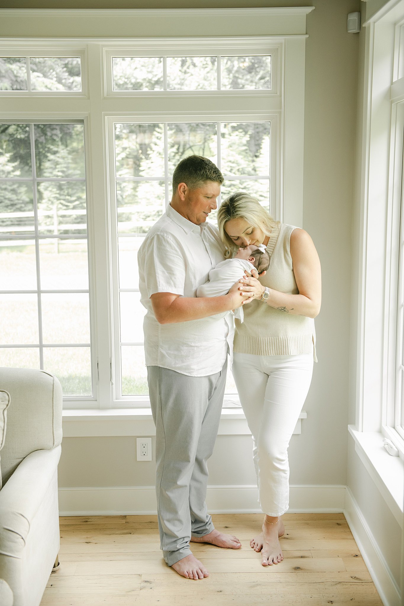 New parents stand in a window snuggling their sleeping newborn baby daughter after benefiting from prenatal yoga lancaster pa