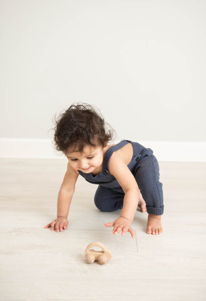 one year old playing with wooden car in studio 
