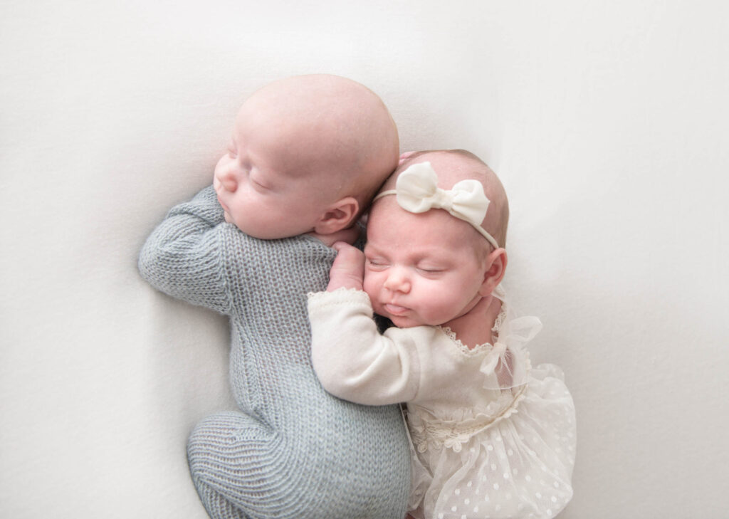 Twin baby newborns posed side by side in adorable outfits in Philadelphia, PA studio 