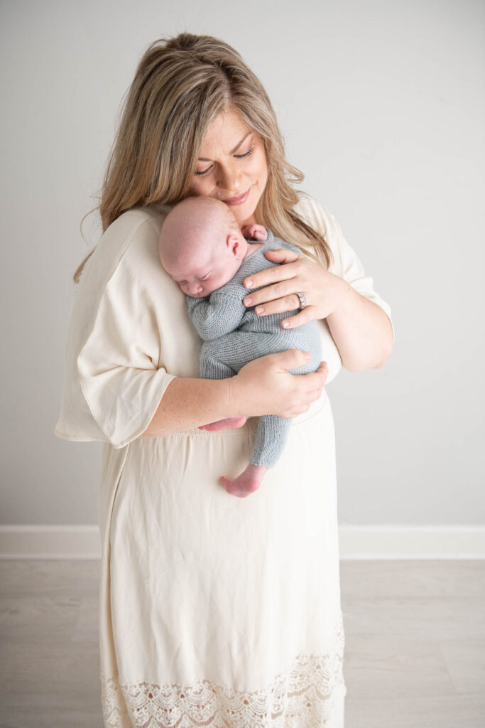 Beautiful mother holding newborn baby boy in cream dress
