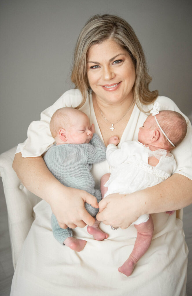 Newborn mother of twins holding twin newborn babies in white dress