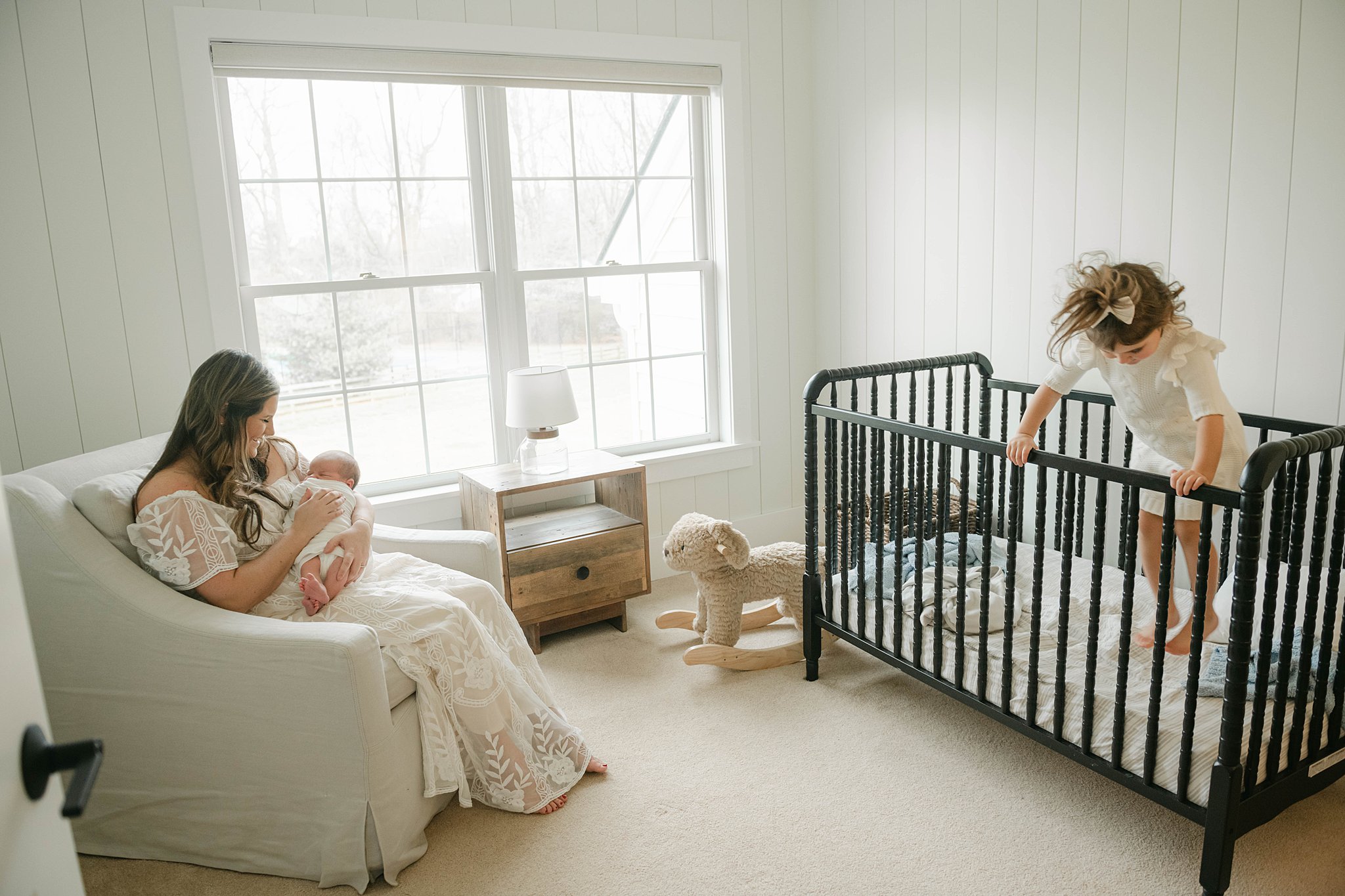 mom sits in nursery armchair holding newborn while older daughter plays in the crib baby stores lancaster pa