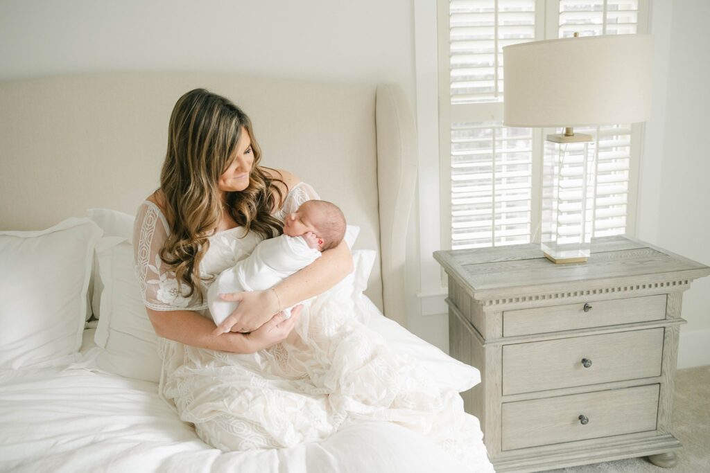 Mother sits on a white bed holding her sleeping newborn