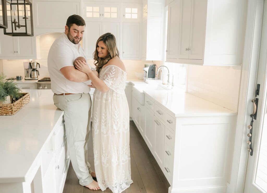 New parents wearing all white stand in a kitchen holding newborn midwives lancaster