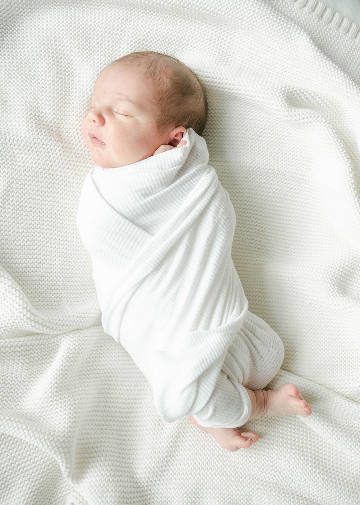 Newborn baby sleeps while swaddled in a white blanket with feet sticking out lancaster doulas