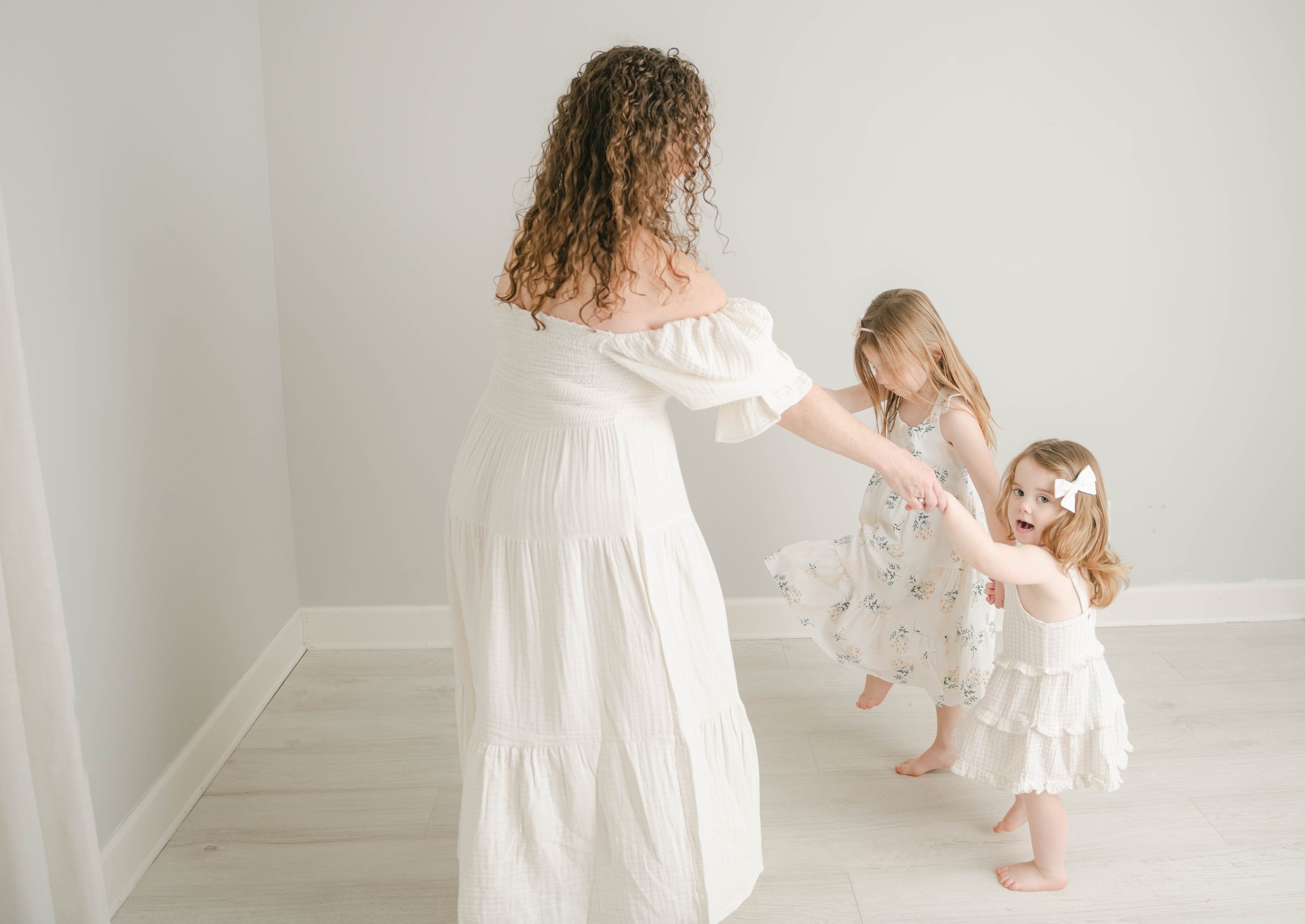 A mother dances while holding hands with her two young daughters