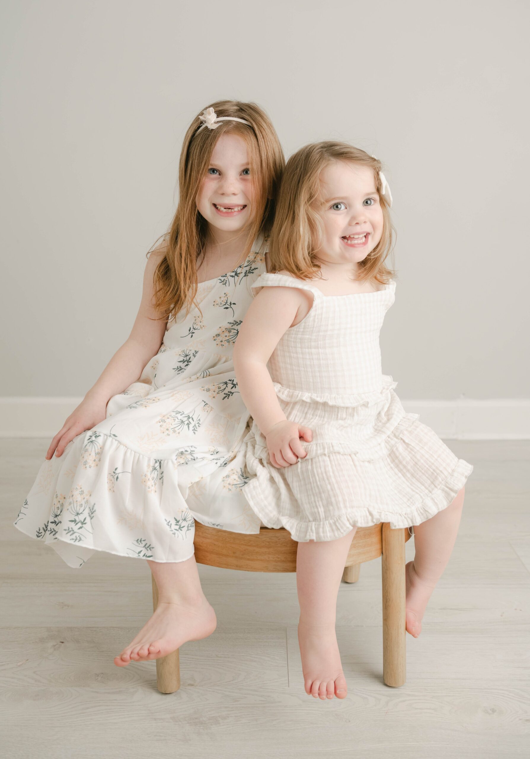 Two sisters sit on a round wooden stool together in a studio bellaboo lancaster