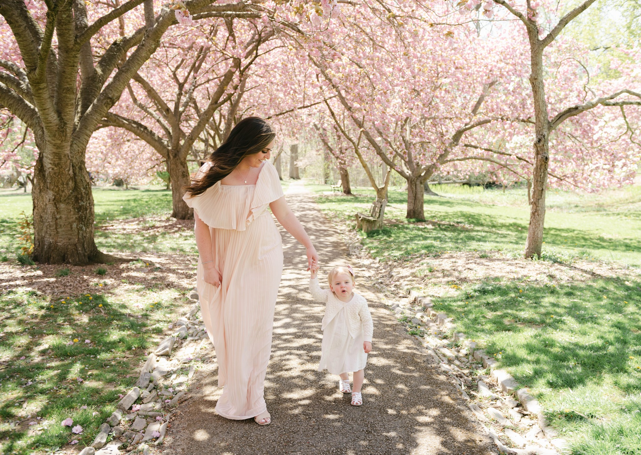 A mother walks her toddler daughter through a path of pink blossom trees h rose boutique