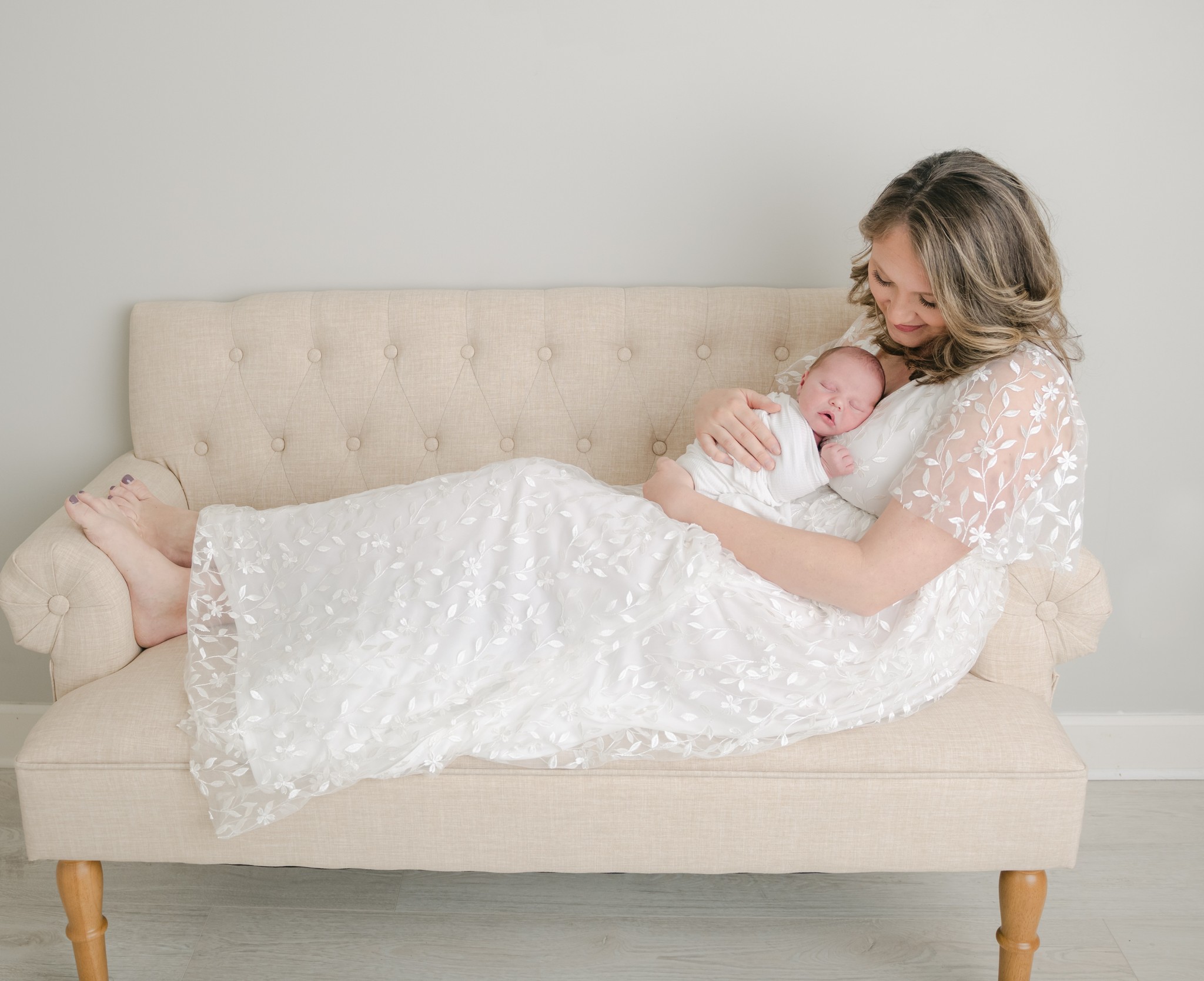 A mother in a lace dress lays across a small couch with her newborn baby sleeping on her chest rising moon midwifery