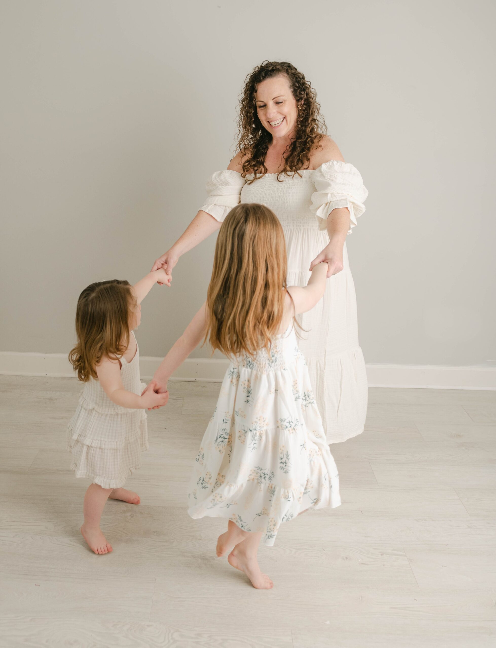 A mother dances with her two young daughters iin white dresses in a studio Chester county obgyn