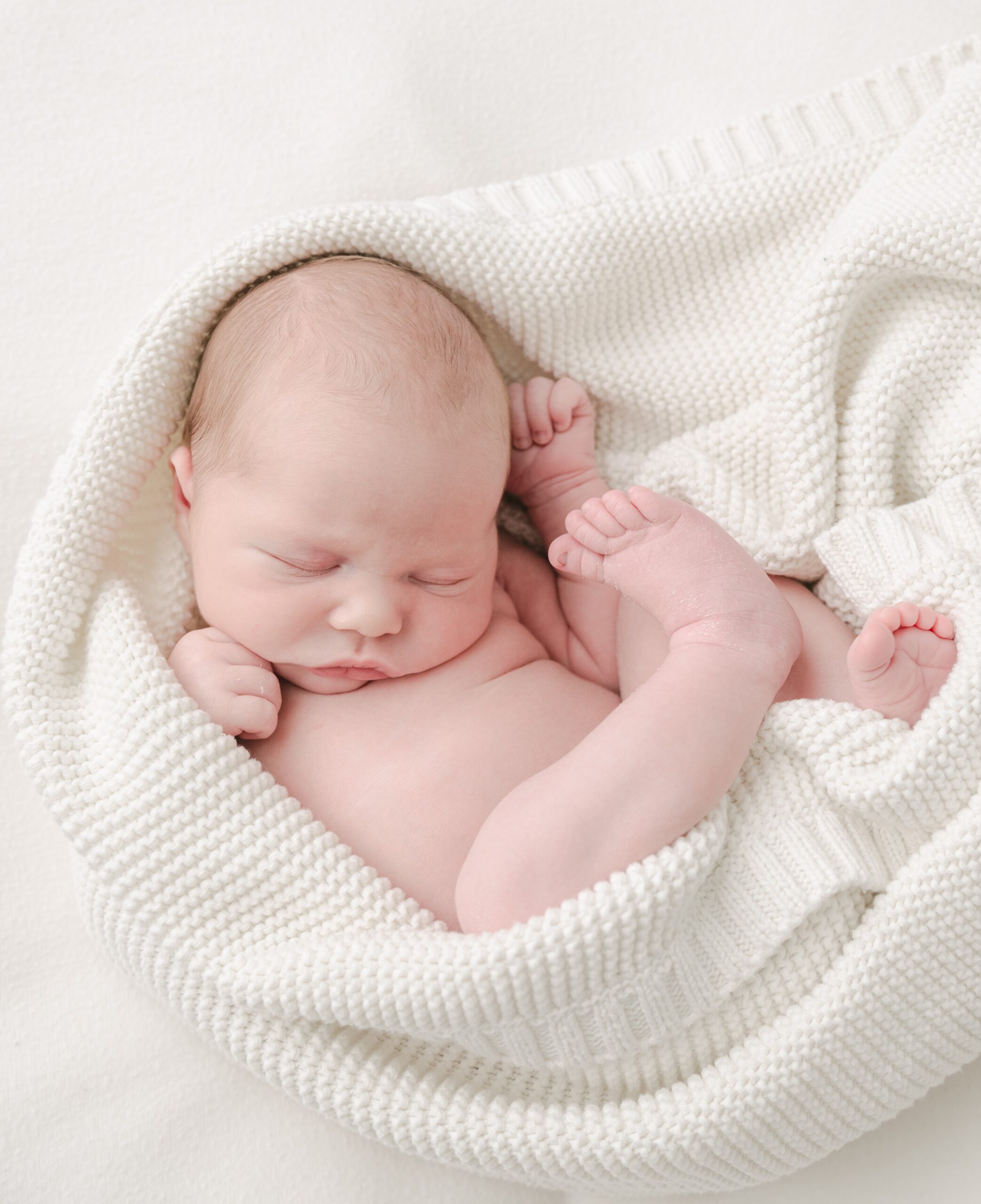 A newborn baby sleeps curled up in a white blanket birth center lancaster pa