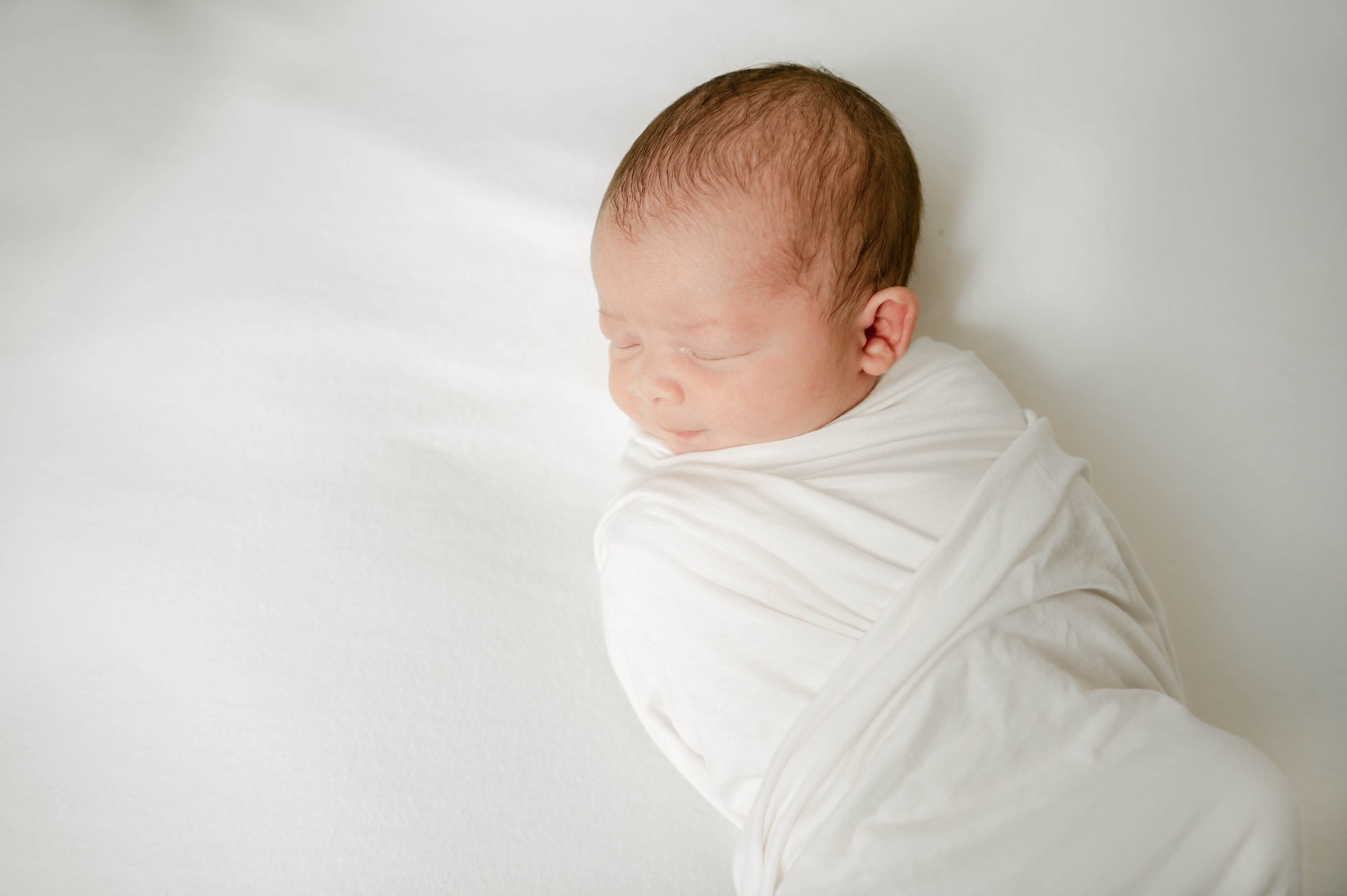 A newborn baby sleeps in a white swaddle lactation consultant lancaster pa