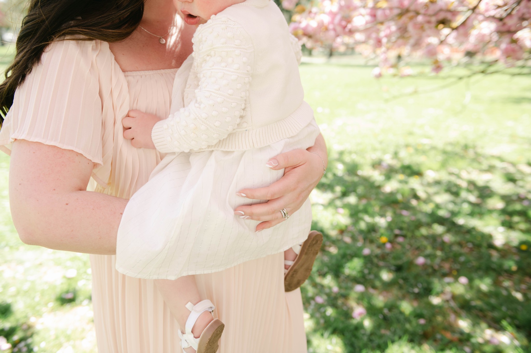 Details of a mother carrying her toddler daughter while walking under a blooming pink tree