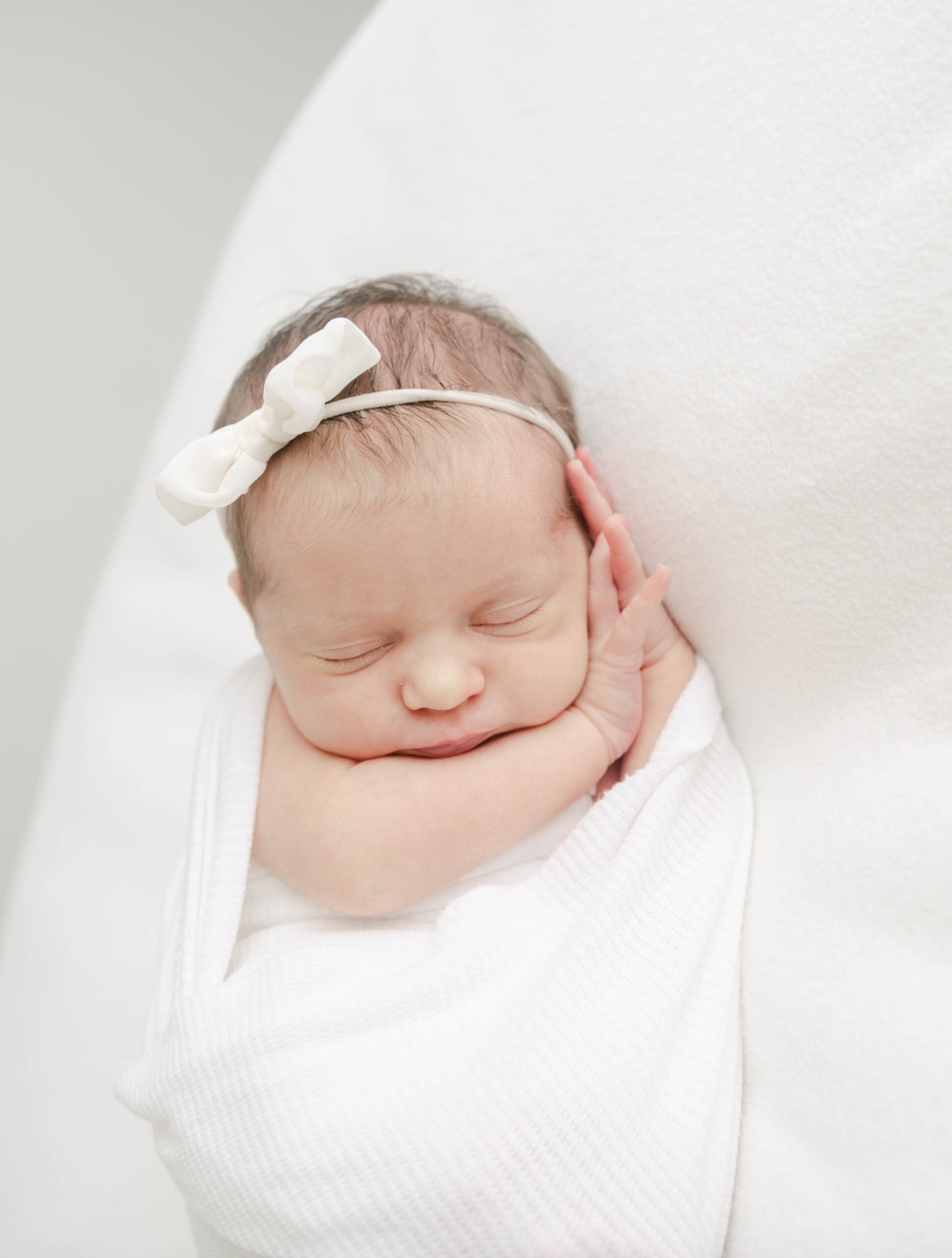 A newborn baby sleeps on her hands in a white swaddle baby boutique west chester pa