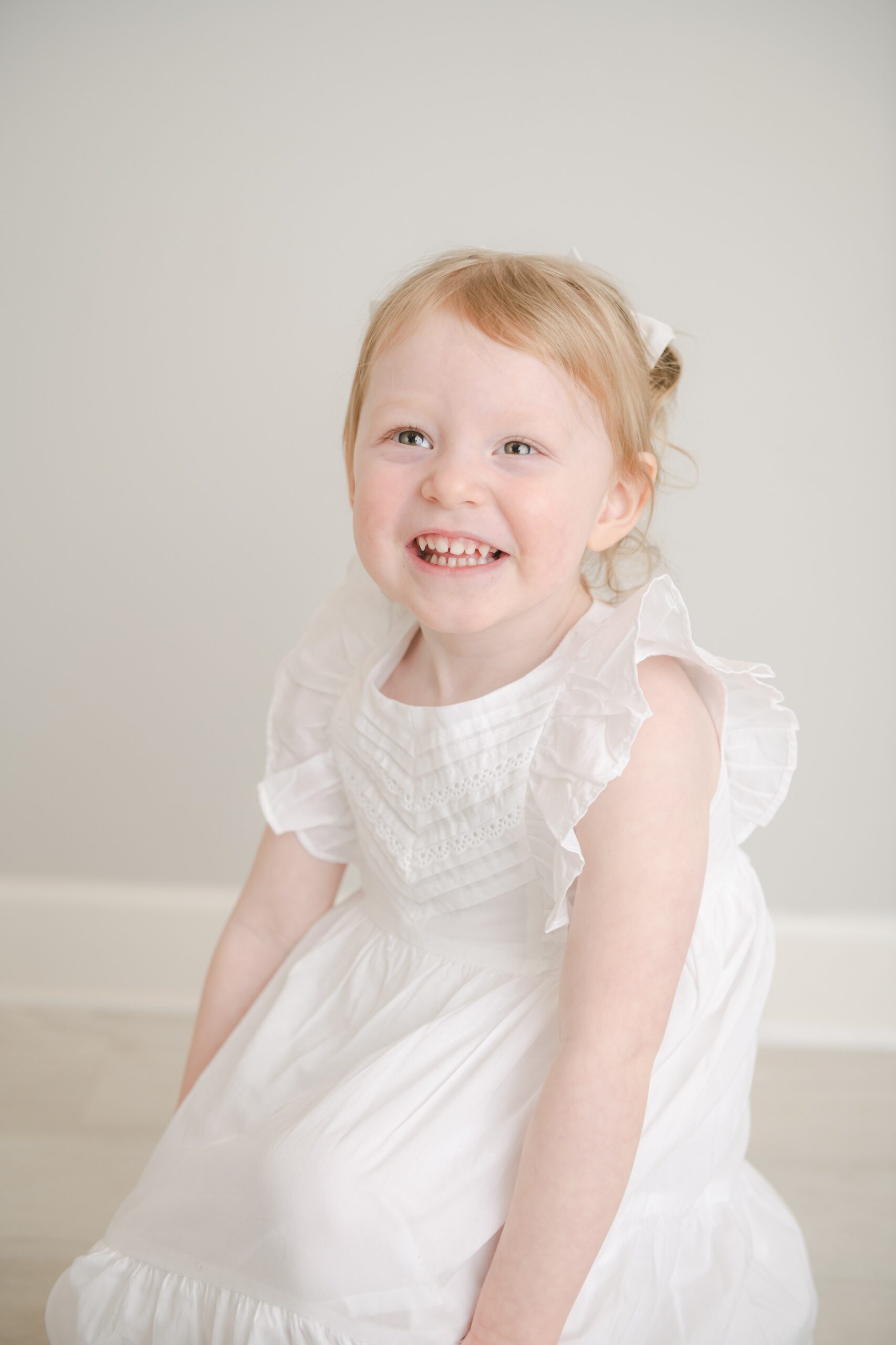A young girl smiles in a white dress while playing in a studio