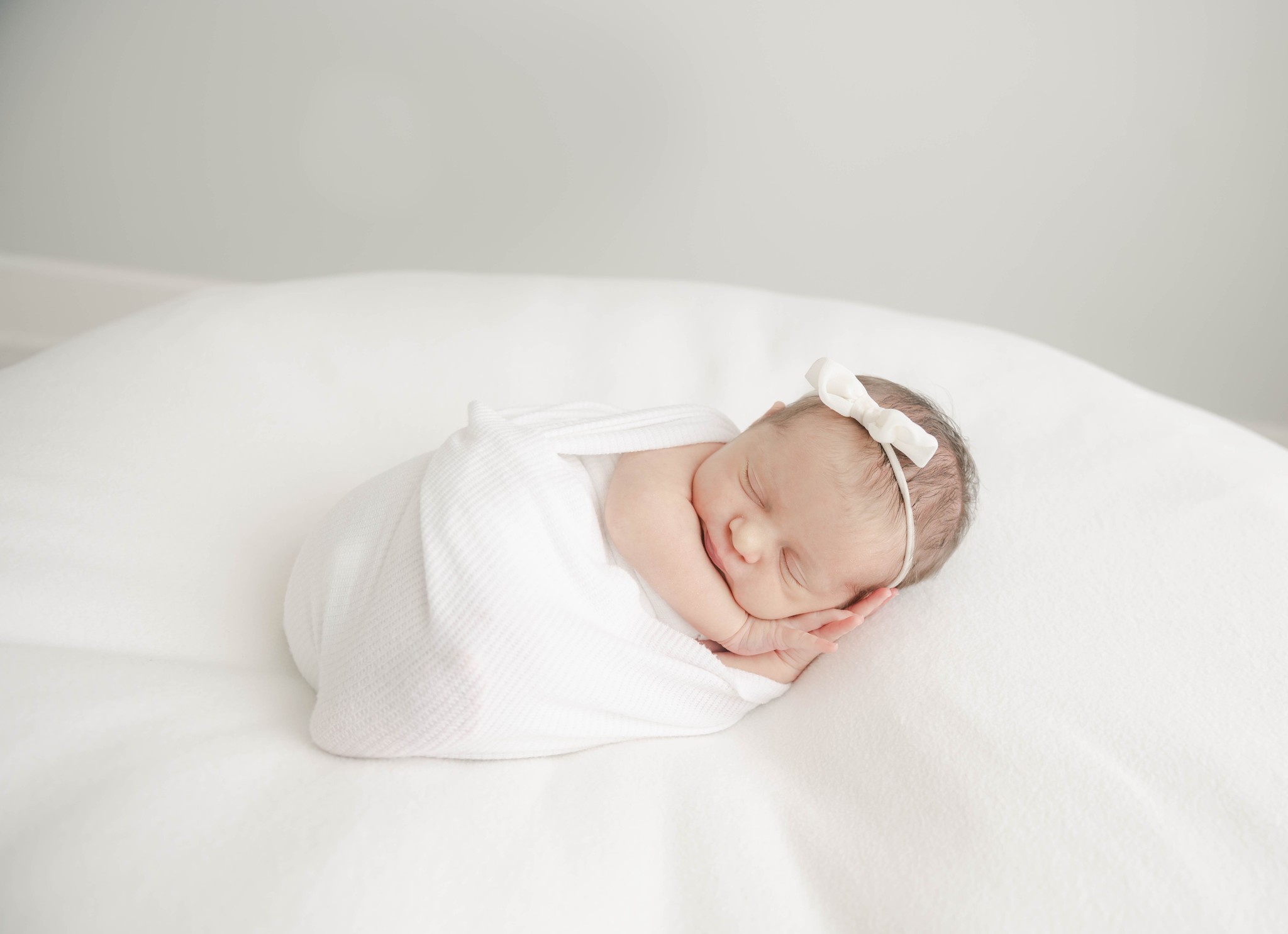 A newborn baby sleeps on her hands in a white swaddle on a white pad in a studio liberty doulas