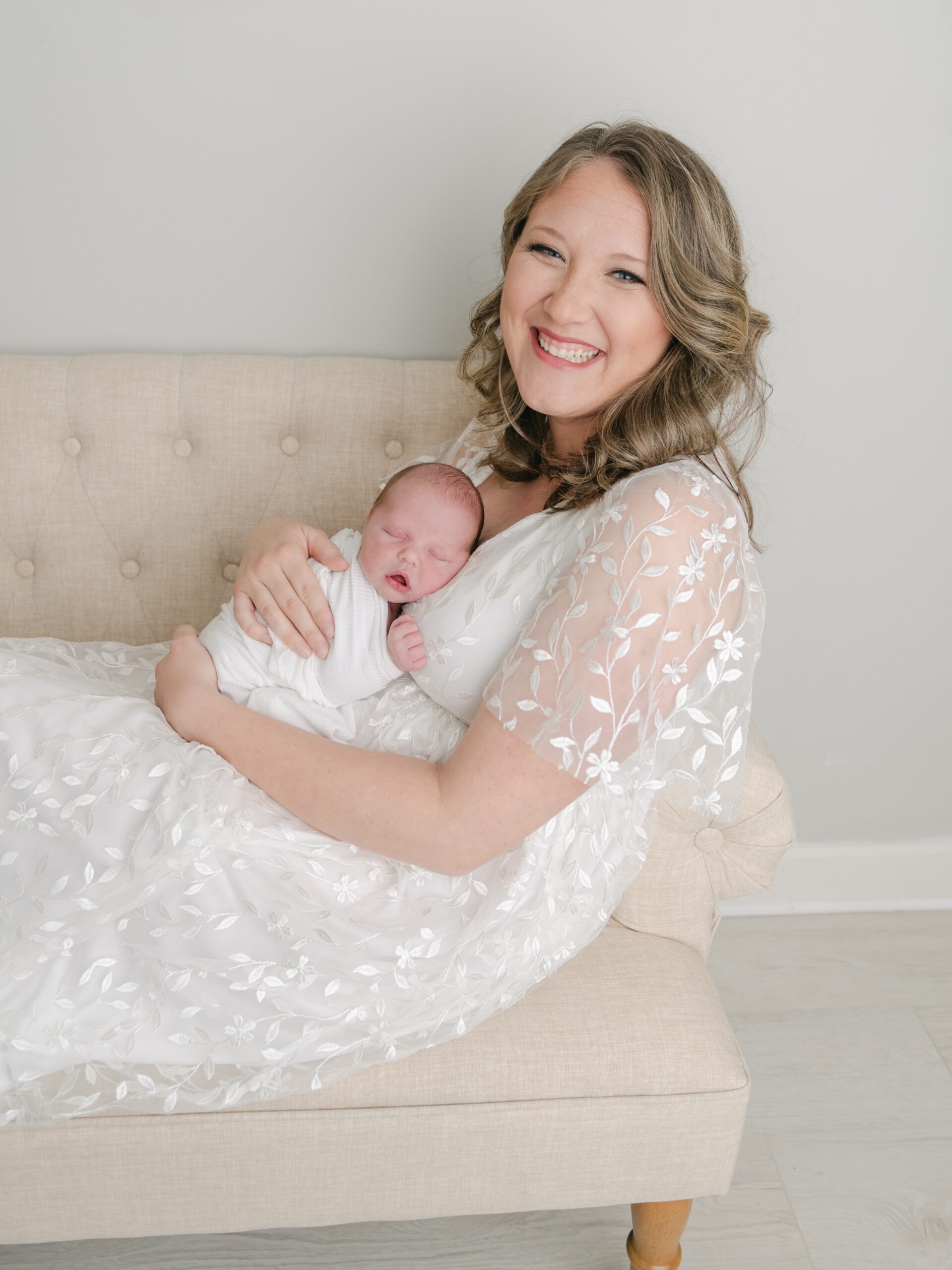 A new mother in a lace maternity gown sits on a couch while her newborn baby sleeps on her chest prenatal massage lancaster pa
