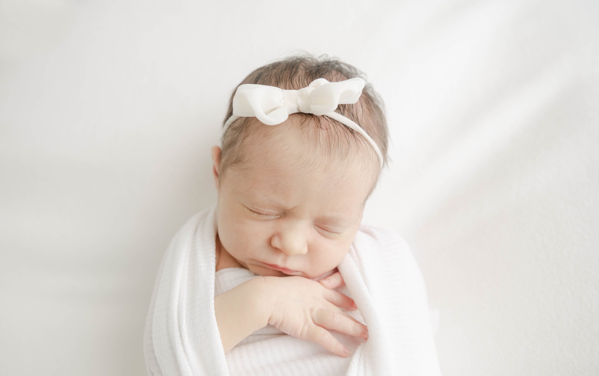Details of a sleeping newborn baby girl in a white swaddle and bow