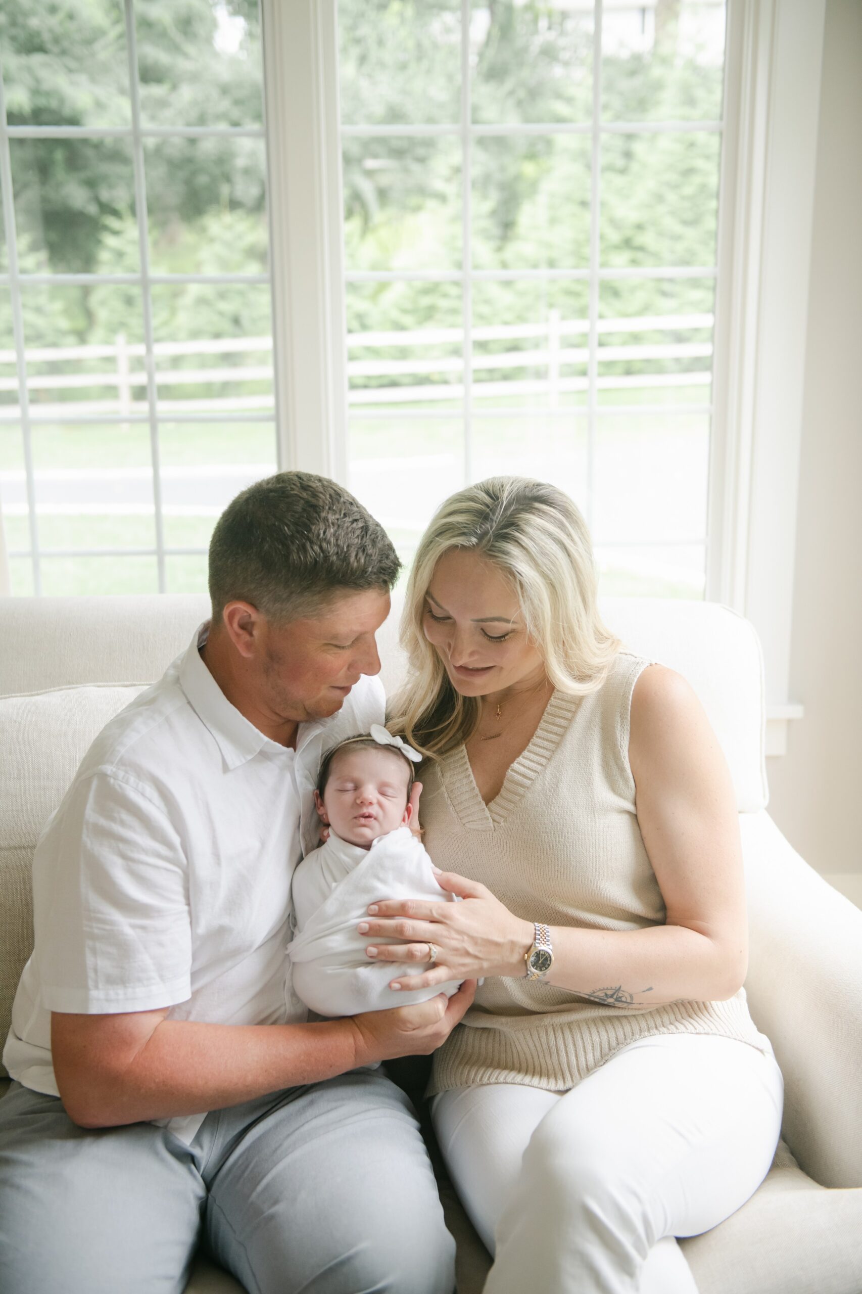 New parents sit on a couch by a window cradling their newborn daughter downington obgyn