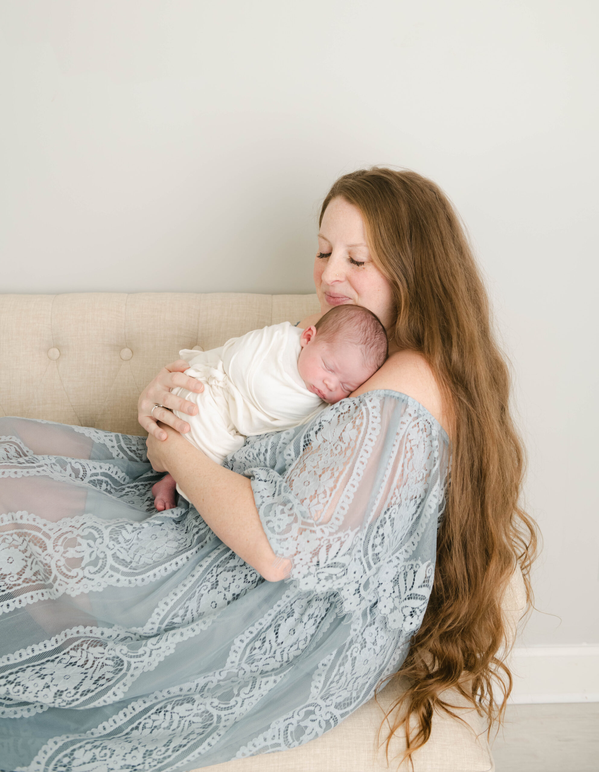 A mom snuggles her sleeping newborn baby while sitting across a couch prenatal yoga west chester pa