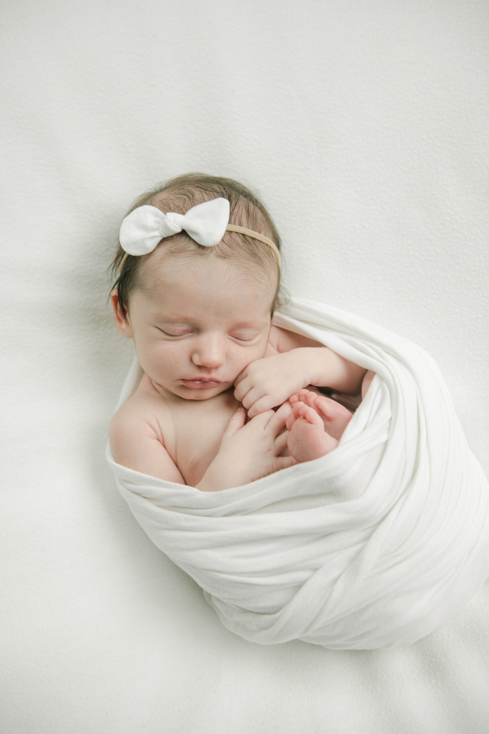 A newborn baby sleeps in a white swaddle on a white bed bryn mawr labor and delivery