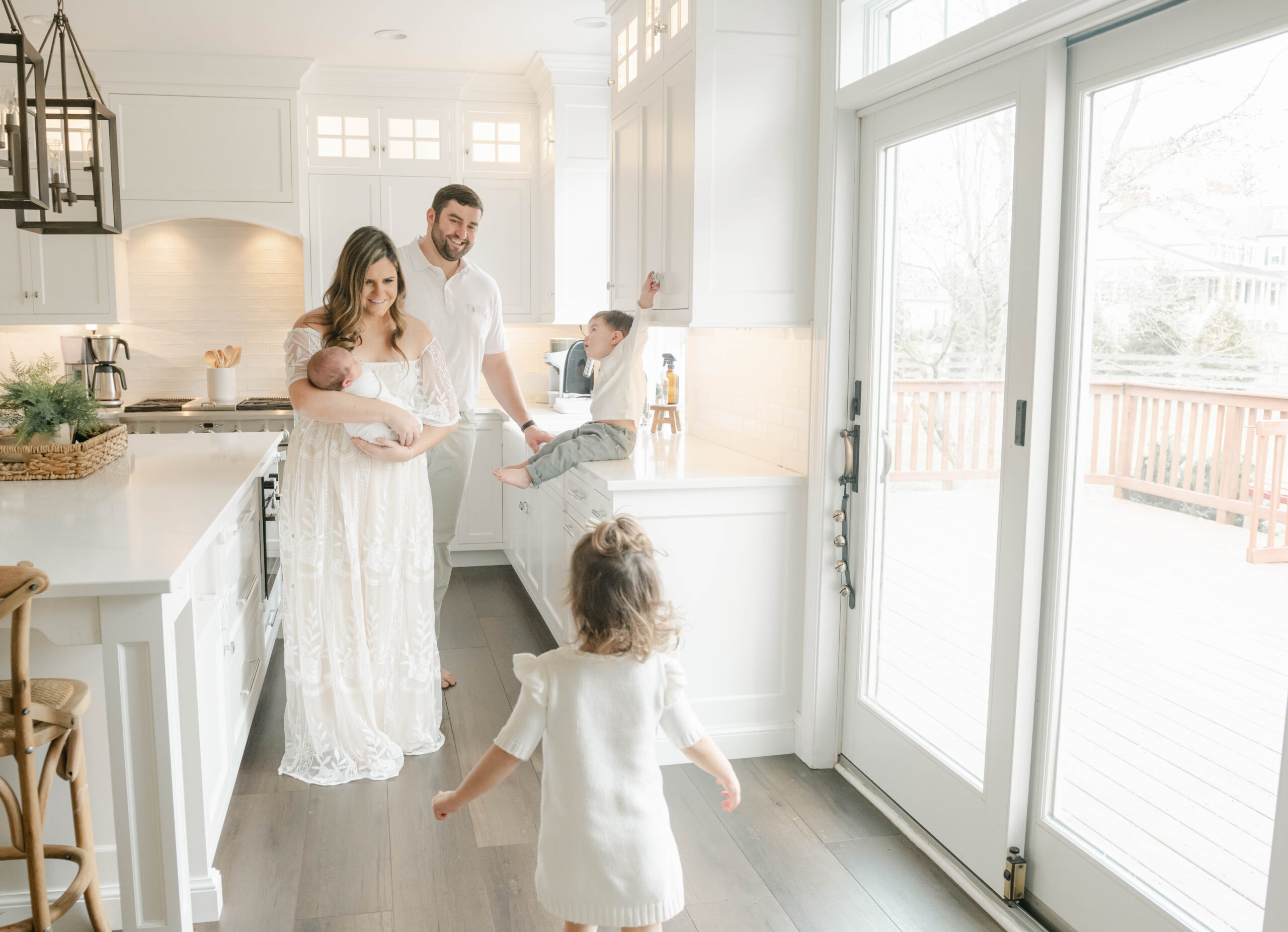 A mother and father play with their two toddler children in their white kitchen as mom holds their newborn baby from maternal fetal medicine west chester