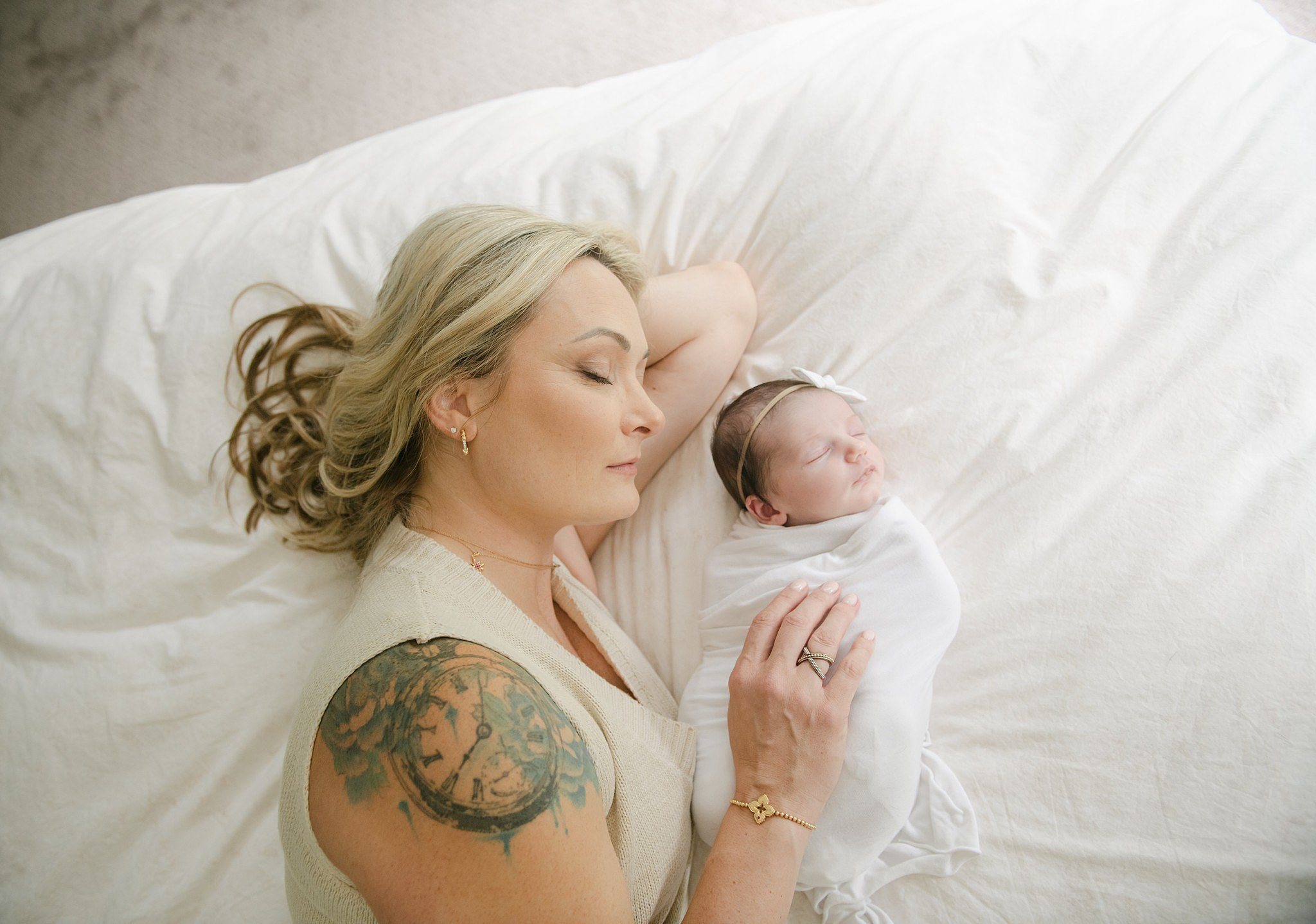 A new mom lays on a bed cuddling with her sleeping newborn daughter